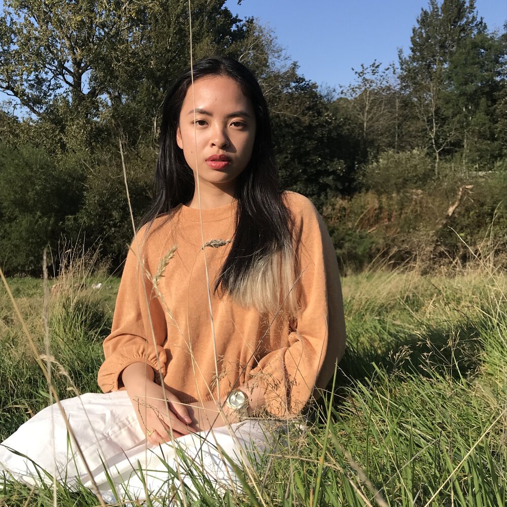 profile image of Nini sitting on grass in the sun.