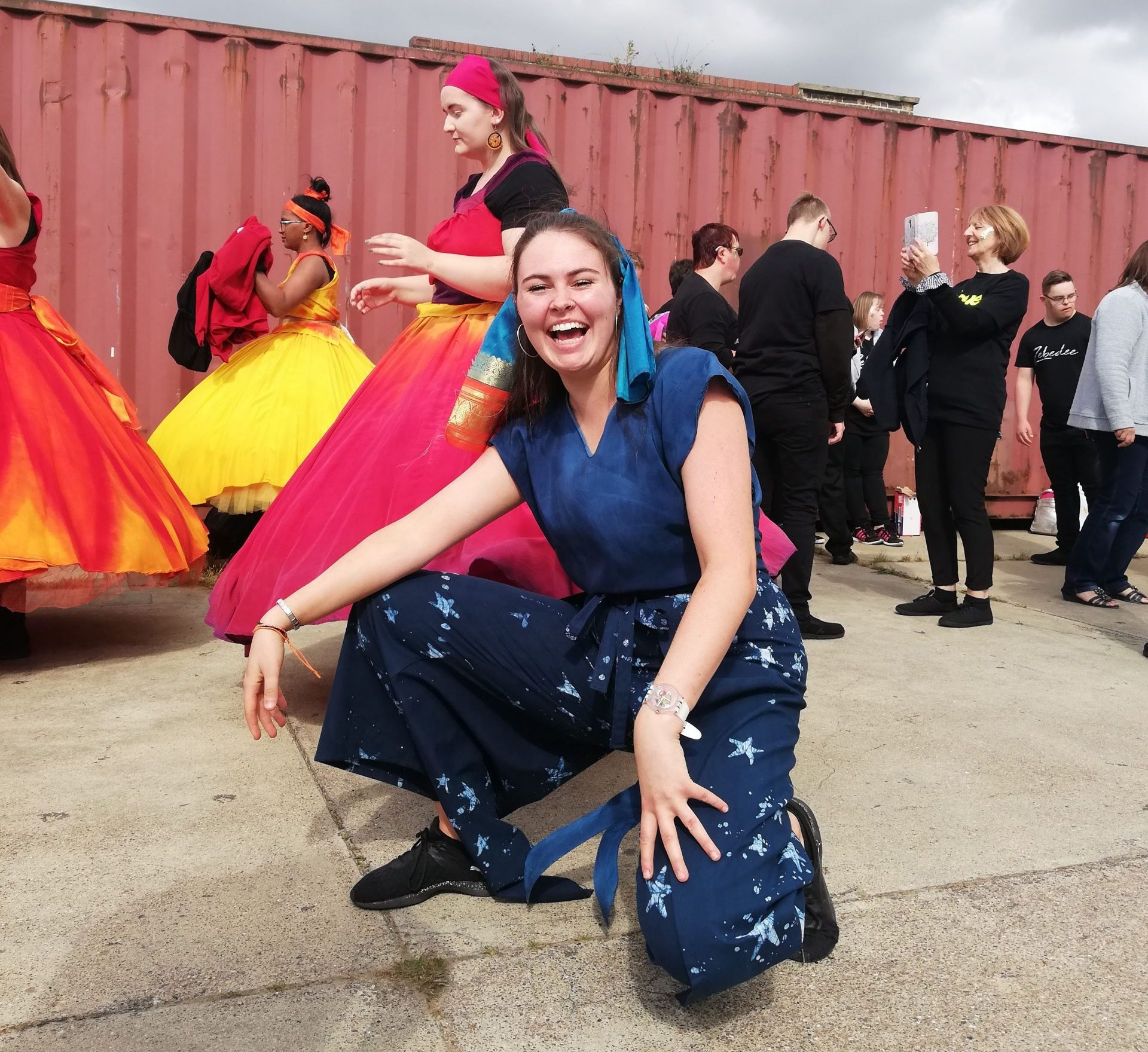 Profile image of Sally Hendry, Company DNA Director, crouching in front of a shipping container with people in costume behind her.