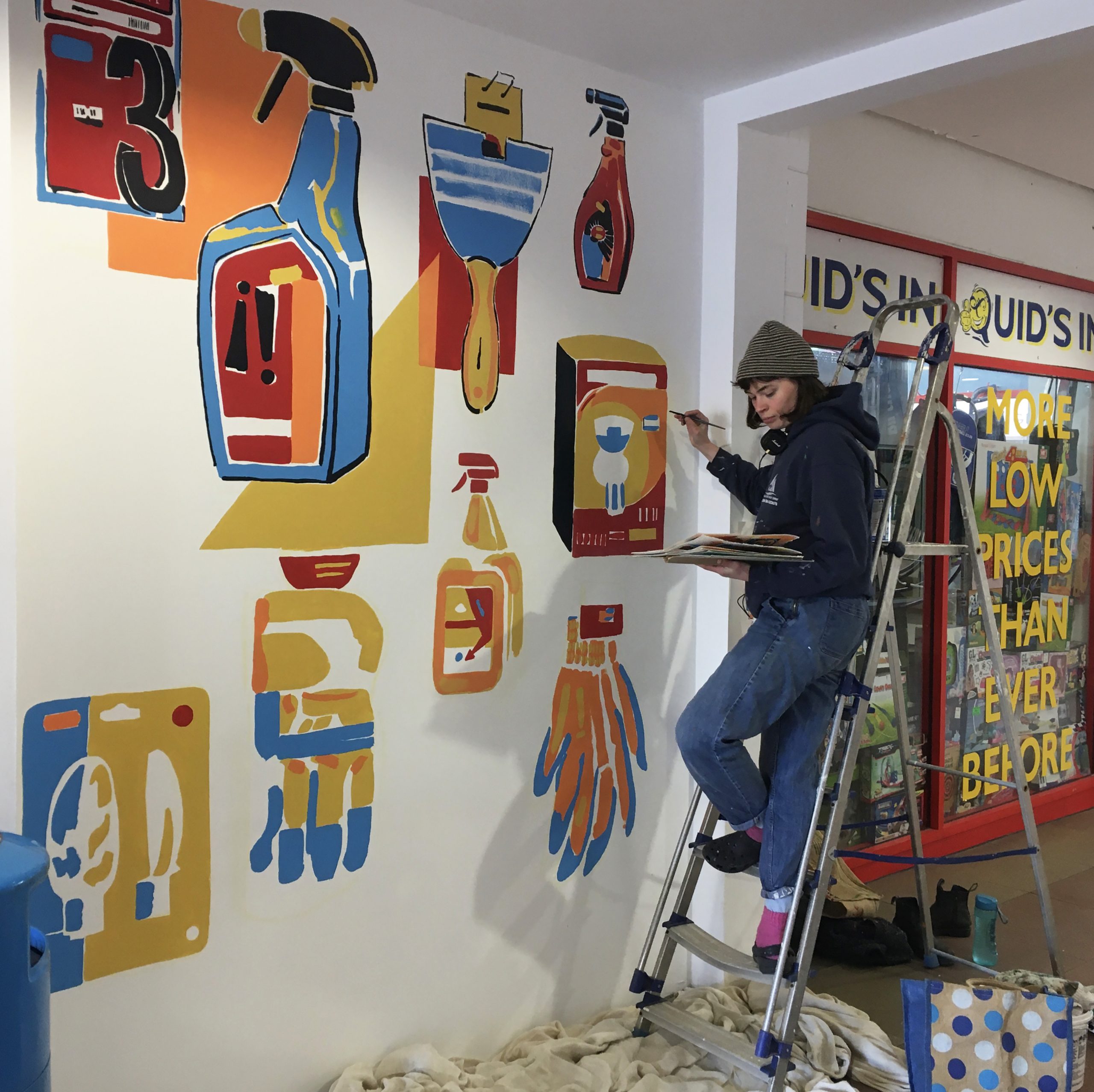 Image showing Jennie painting a large, bright and colourful mural indoors.